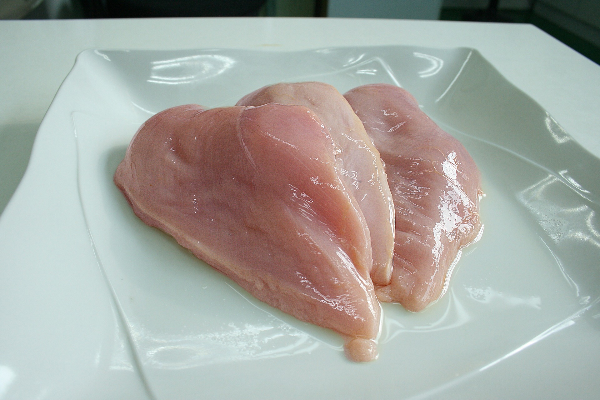 Two raw chicken breasts on a white plate
